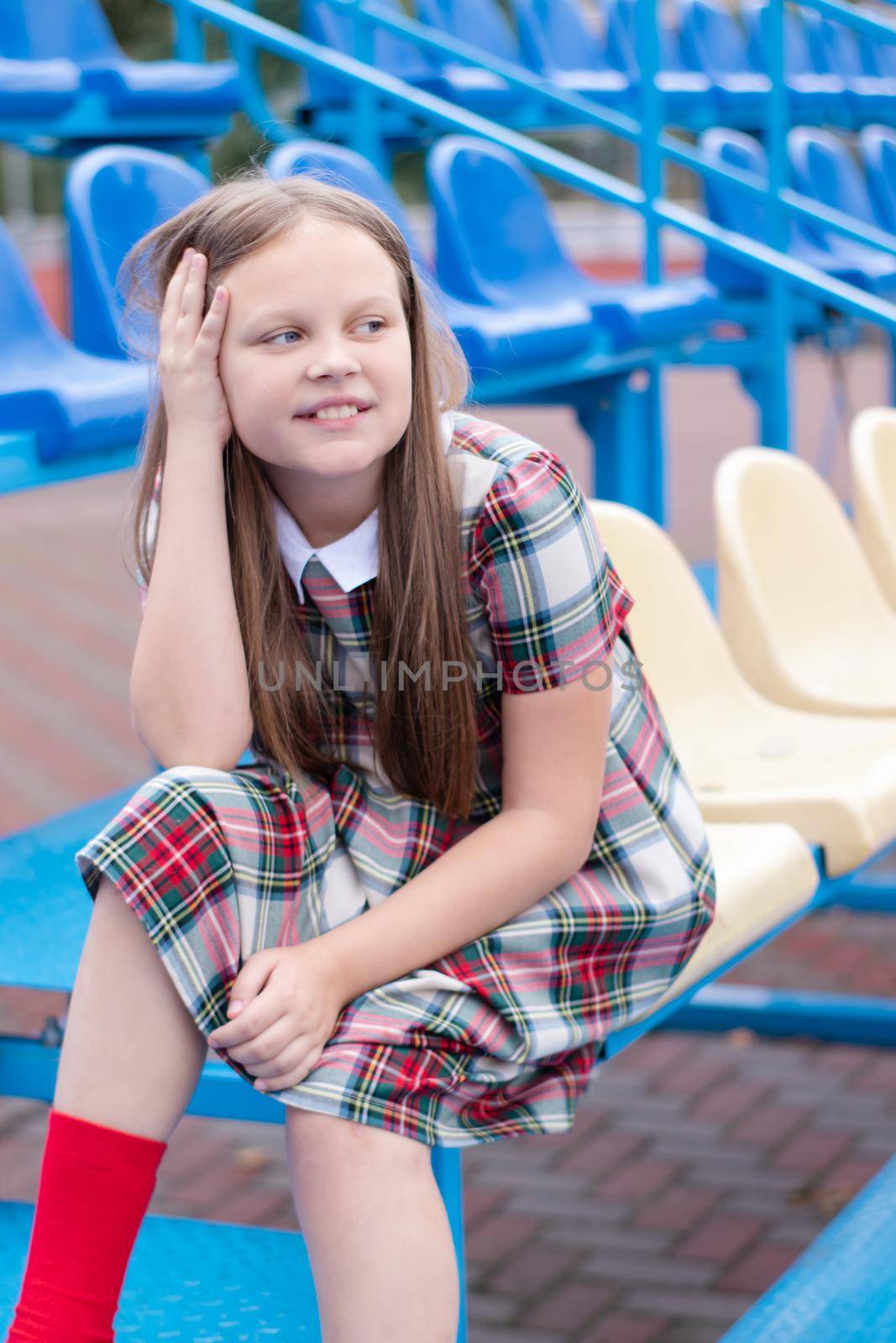 pretty girl in school dress uniform on the blue and yellow tribune of the school stadium. school time. tween. by oliavesna