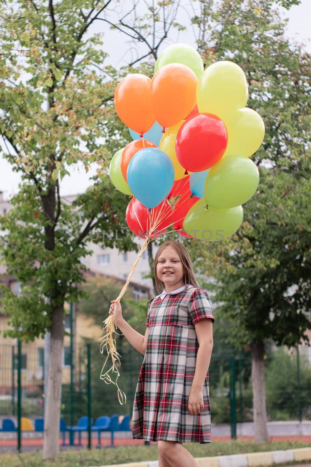 charming teenage girl in checkered brown dress with bunch of colorful balloons. school girl. pretty tween by oliavesna