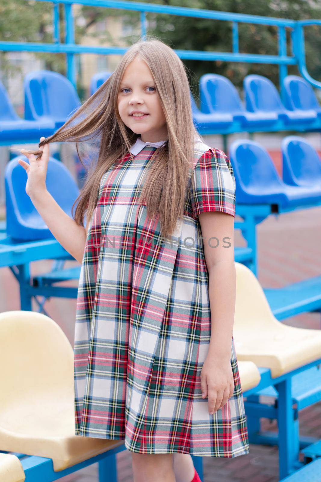 pretty girl in school dress uniform on the blue and yellow tribune of the school stadium. school time. tween. by oliavesna