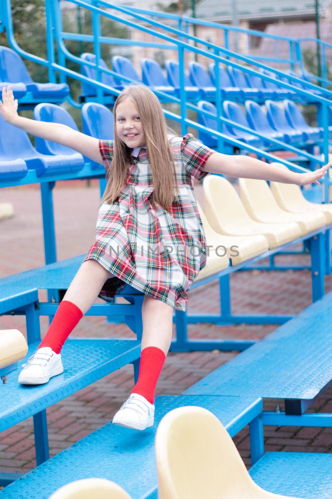 pretty girl in school dress uniform on the blue and yellow tribune of the school stadium. school time. tween