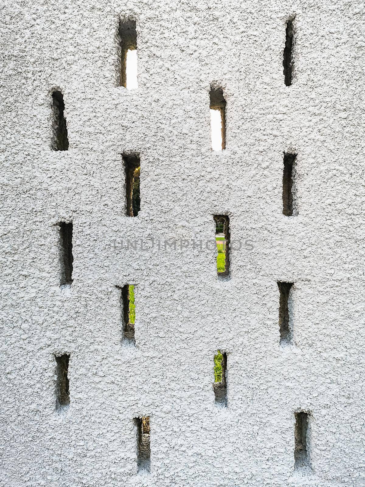 Part of big concrete fence in park with small oblong holes inside 