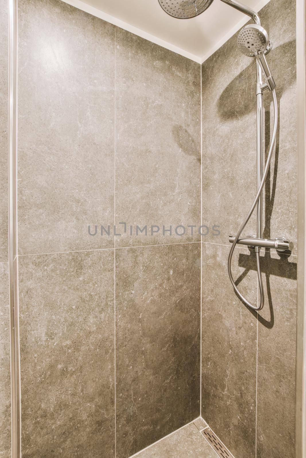 Shower faucets attached to tiled wall near glass partition and ornamental curtail in washroom at home