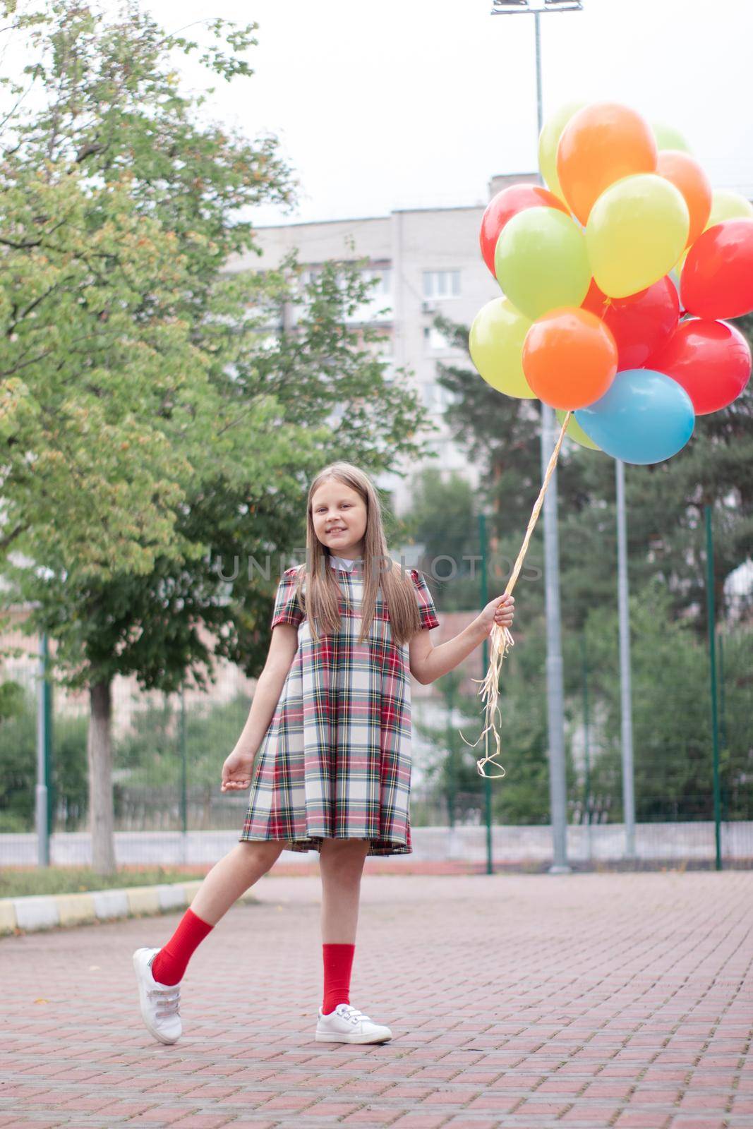 charming teenage girl in checkered brown dress with bunch of colorful balloons. school girl. pretty tween.