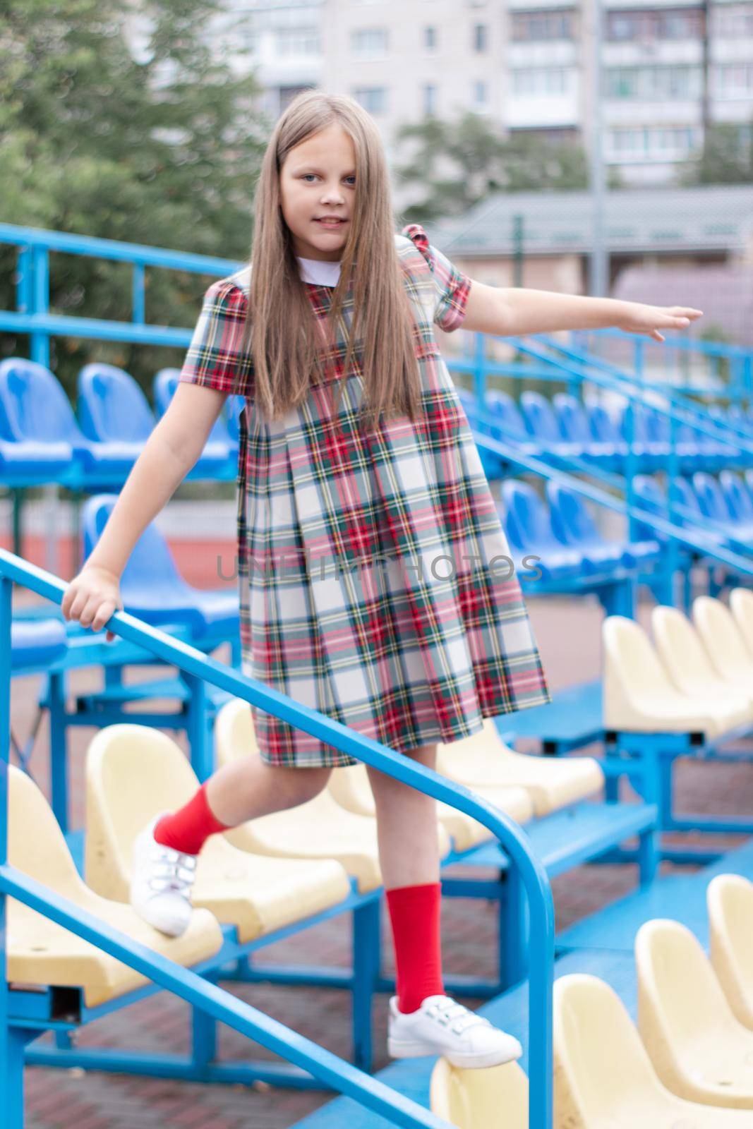 pretty girl in school dress uniform on the blue and yellow tribune of the school stadium. school time. tween. by oliavesna