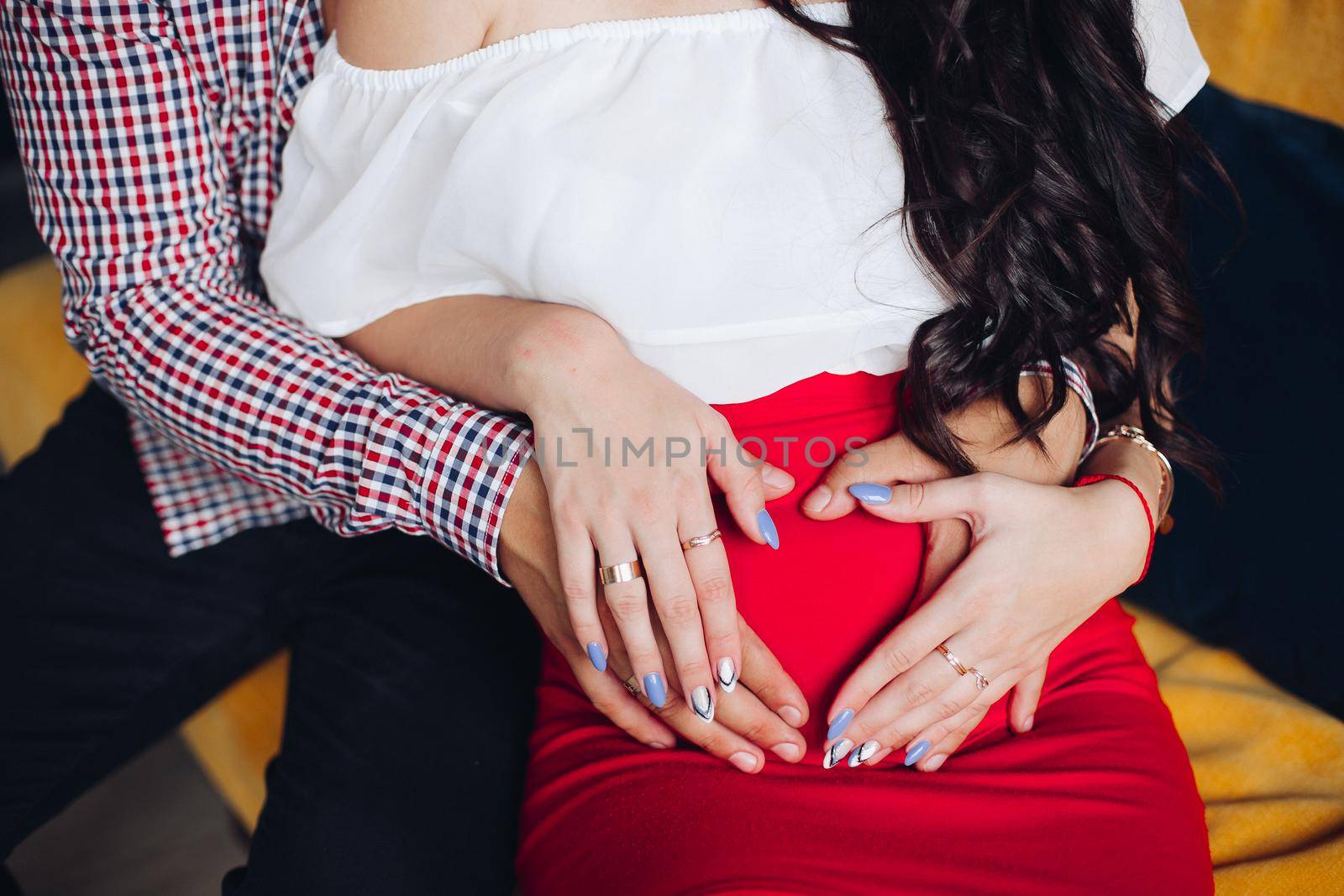 Expecting husband and wife embracing her belly making heart shape with their hands. Waiting for a baby concept.