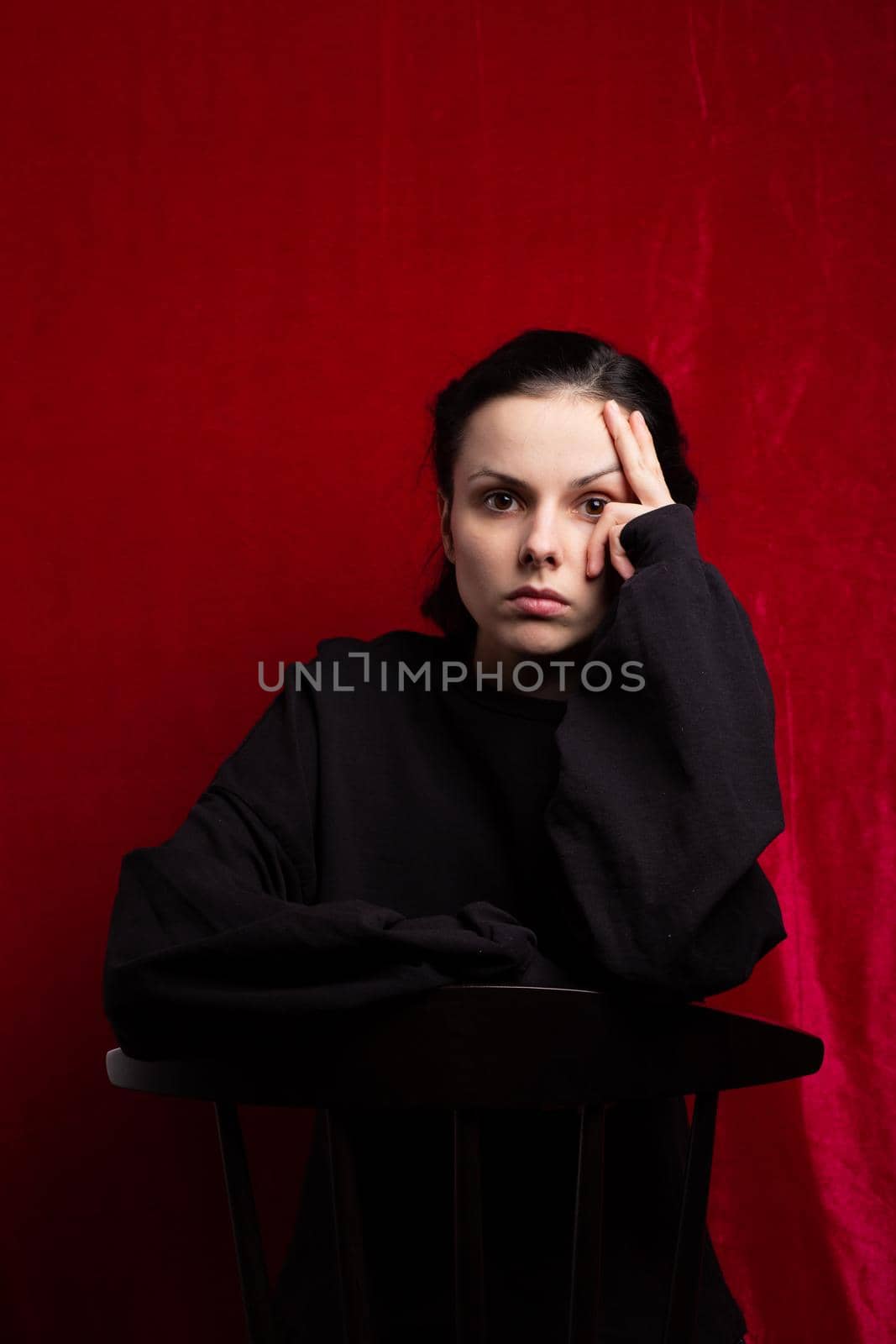 a woman in a black sweater sits at a chair, red background. High quality photo