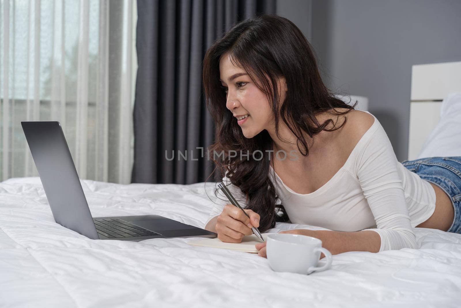 woman writing notebook and using laptop computer on a bed