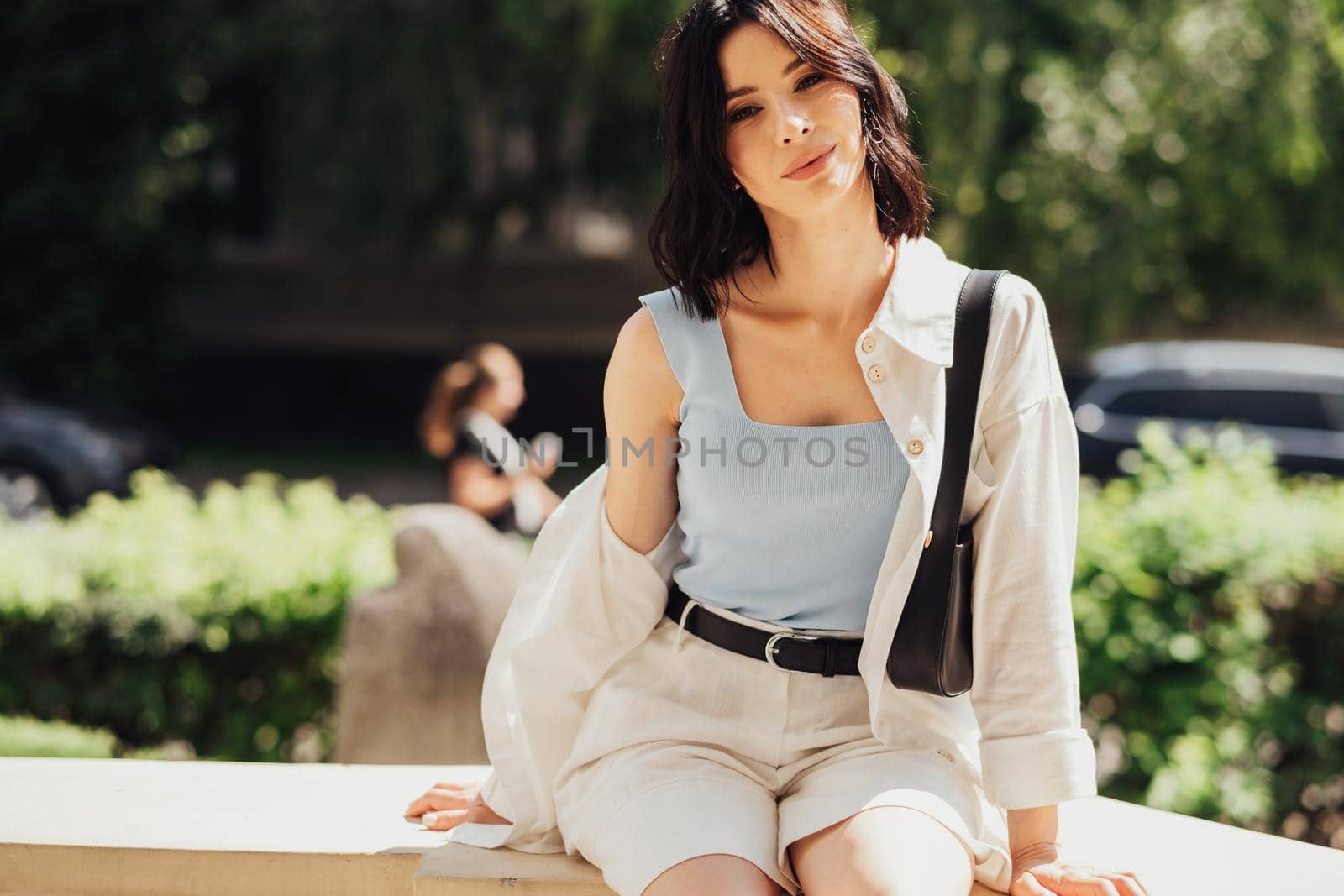 Portrait of Fashionable Young Brunette Woman Posing While Sitting on Handrail Outdoors