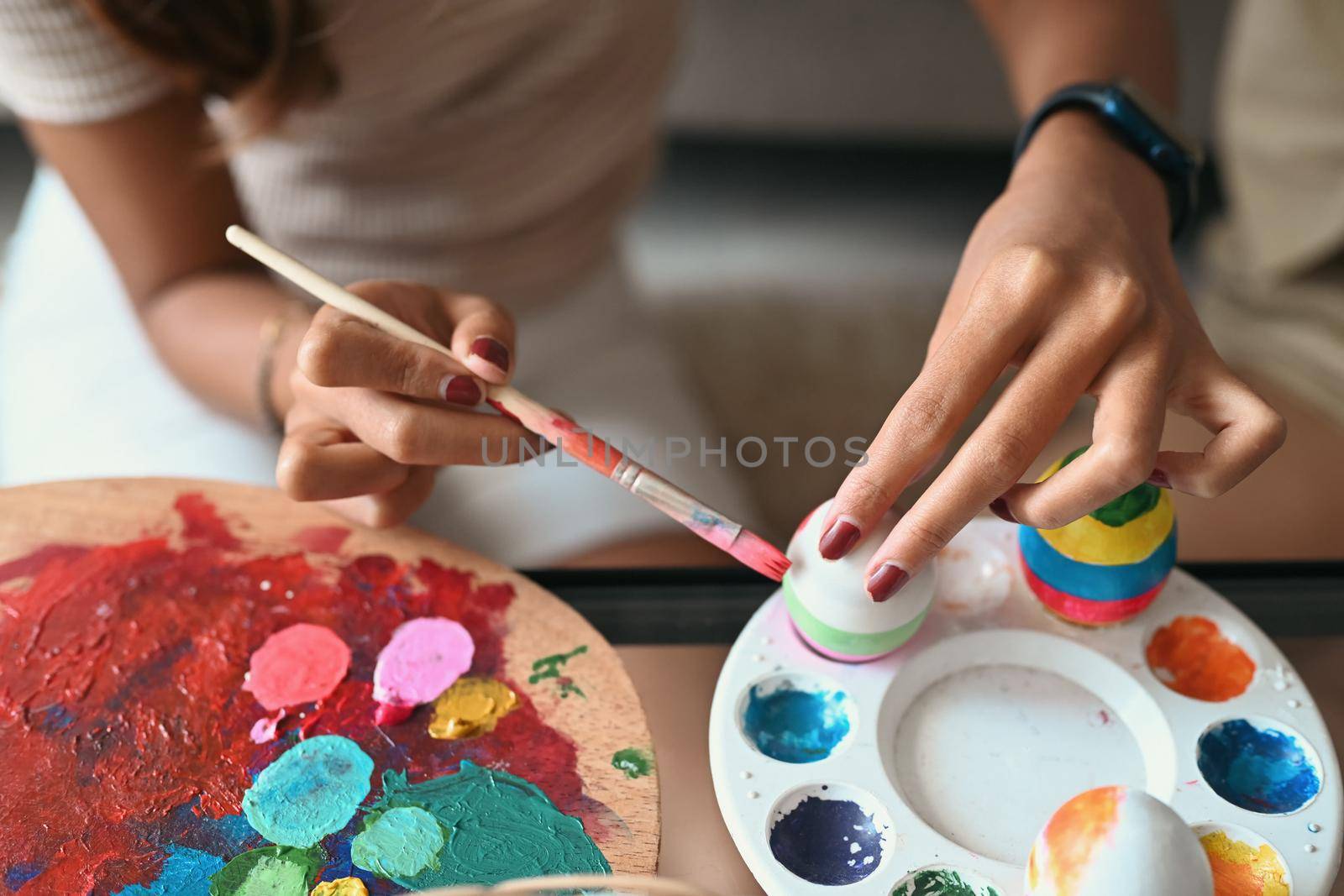 Cropped image of young woman coloring Easter eggs with colors and brush. Easter, holidays and people concept.