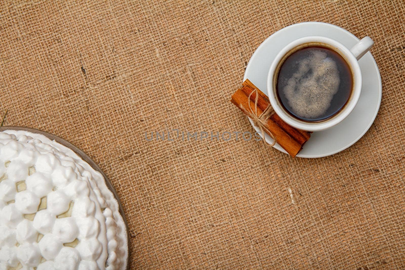 Cup of coffee, cinnamon and biscuit cake decorated with whipped cream on table with sackcloth. Top view