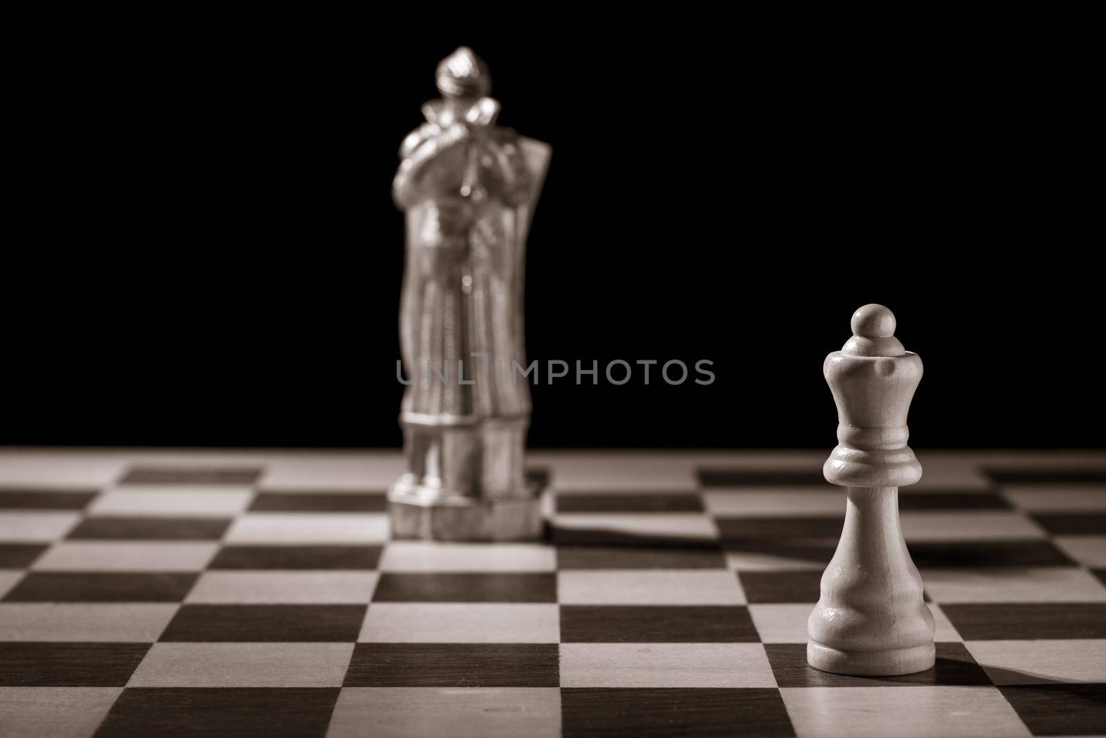 Classic white queen and the same chess piece in the form of medieval figure on the background. Selective focus on classic piece