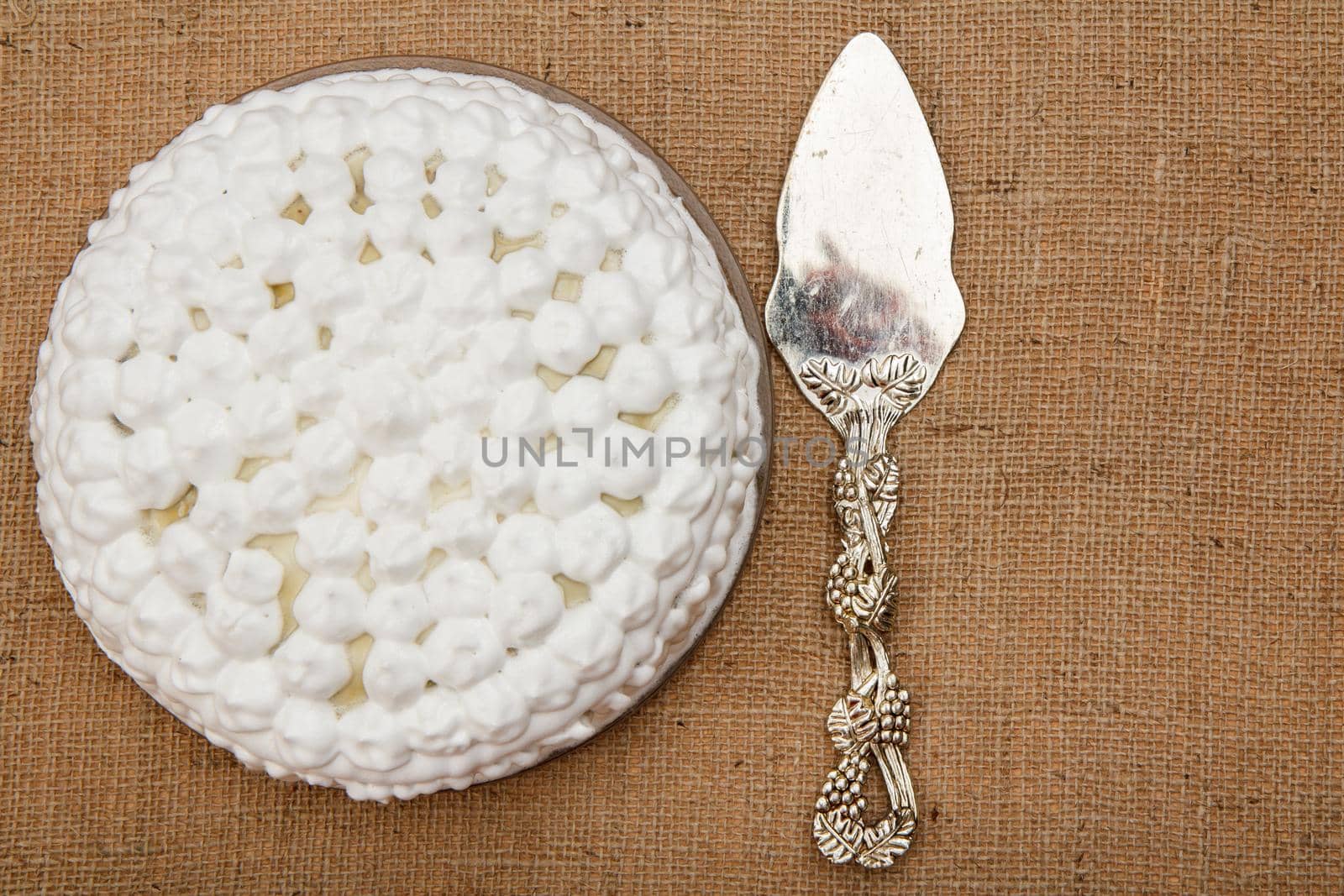 Biscuit cake decorated with whipped cream and silver cake lifter beside it on table with sackcloth. Top view with copy space