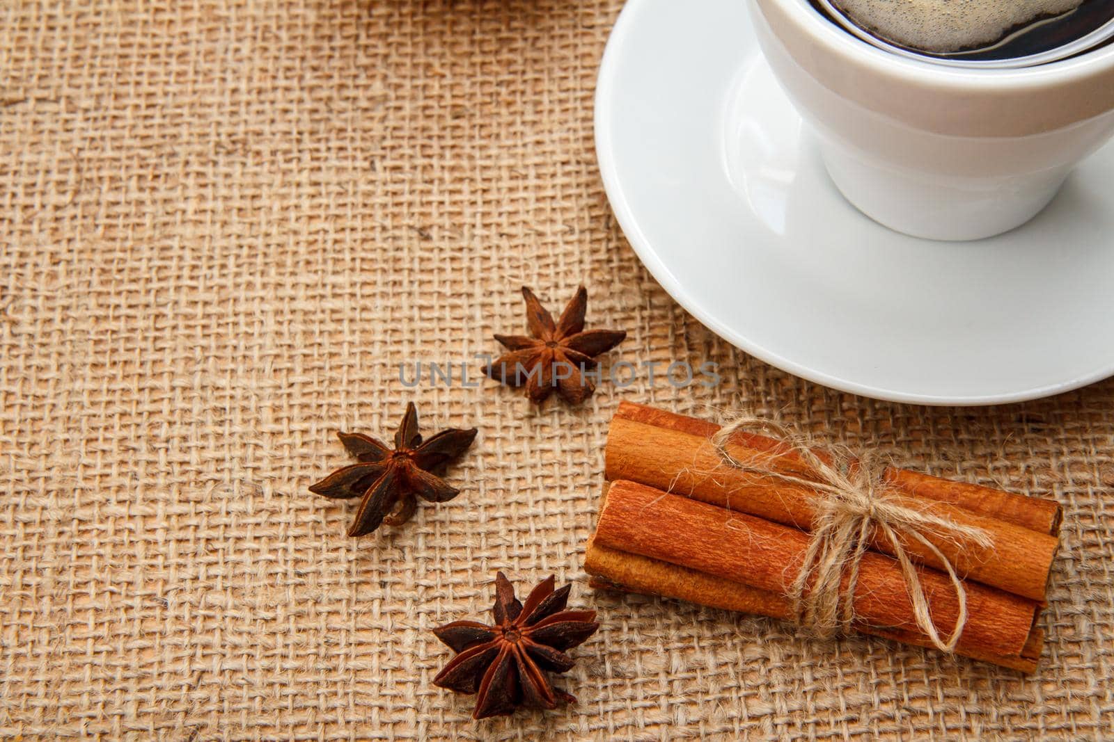Star anise, cinnamon and cup of black coffee on table with sackcloth