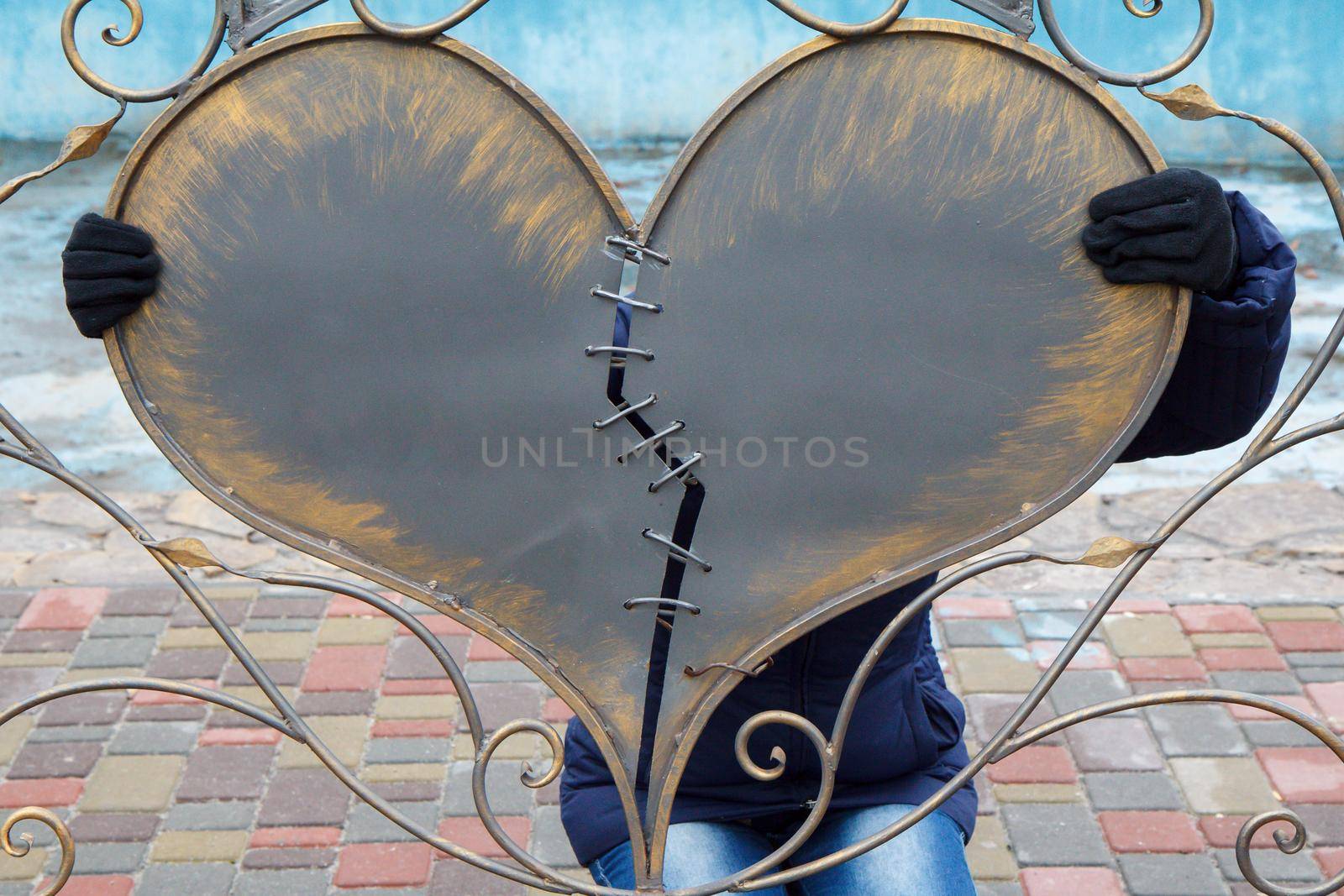 Lady holds broken and sewn together two part of large metal heart