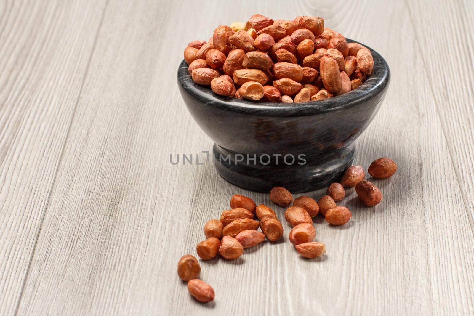 Peanuts in black porcelain bowl and beside it on grey wooden background