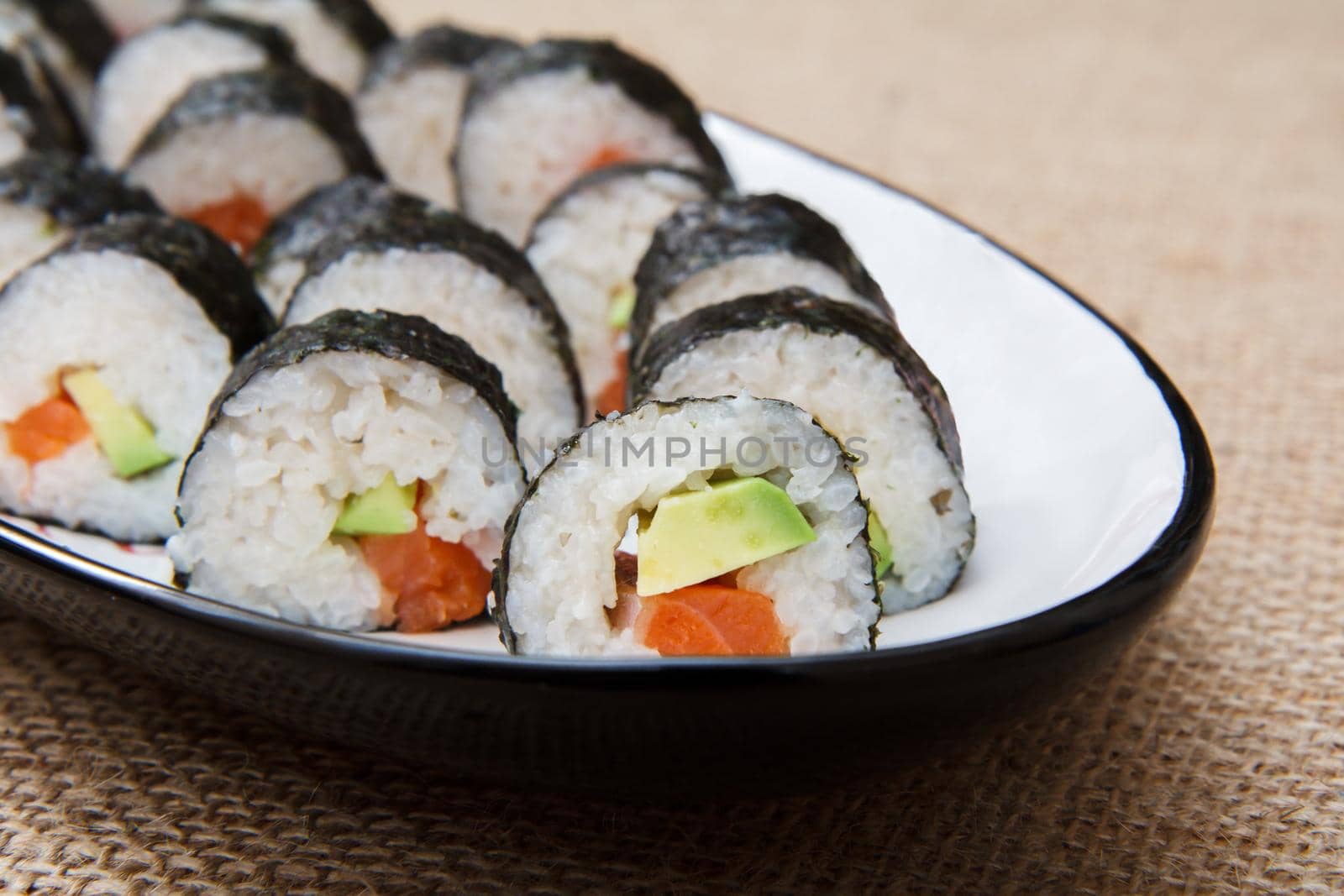 Sushi rolls in nori seaweed sheets with avocado and red fish on ceramic plate on sackcloth