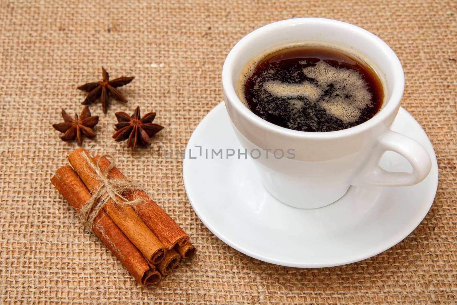 Cup of coffee, star anise and cinnamon on table with sackcloth. Top view