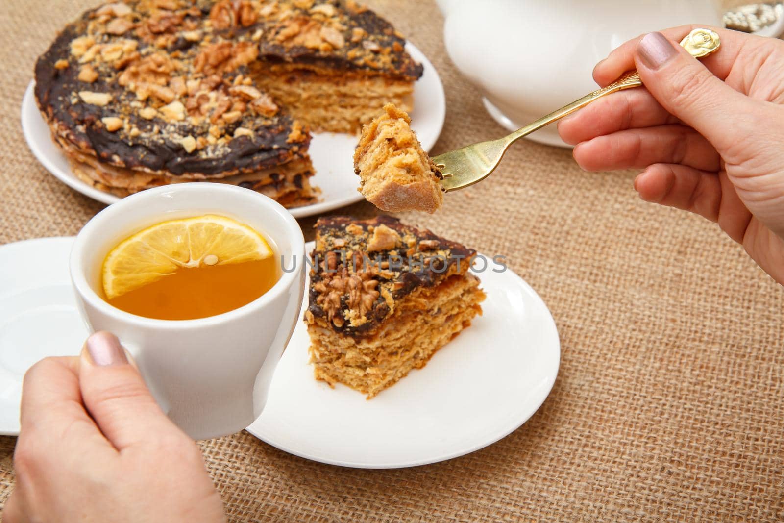 Female hands holding a cup of tea with slice of lemon and fork and going to taste homemade chocolate cake