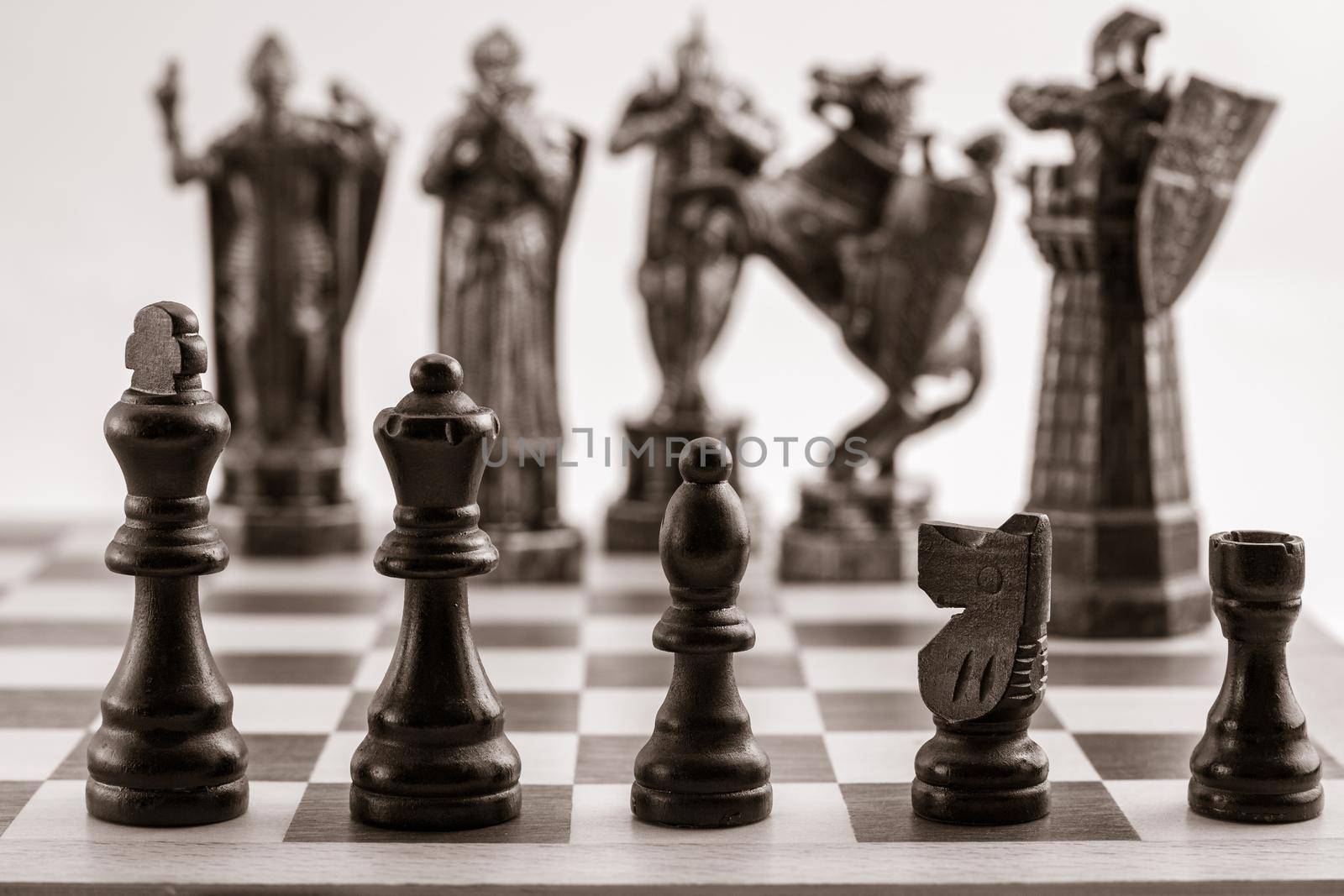 Classic black chess pieces such as king, queen, bishop, knight, rook and the same pieces in the form of medieval figures on the background. Selective focus on classic pieces