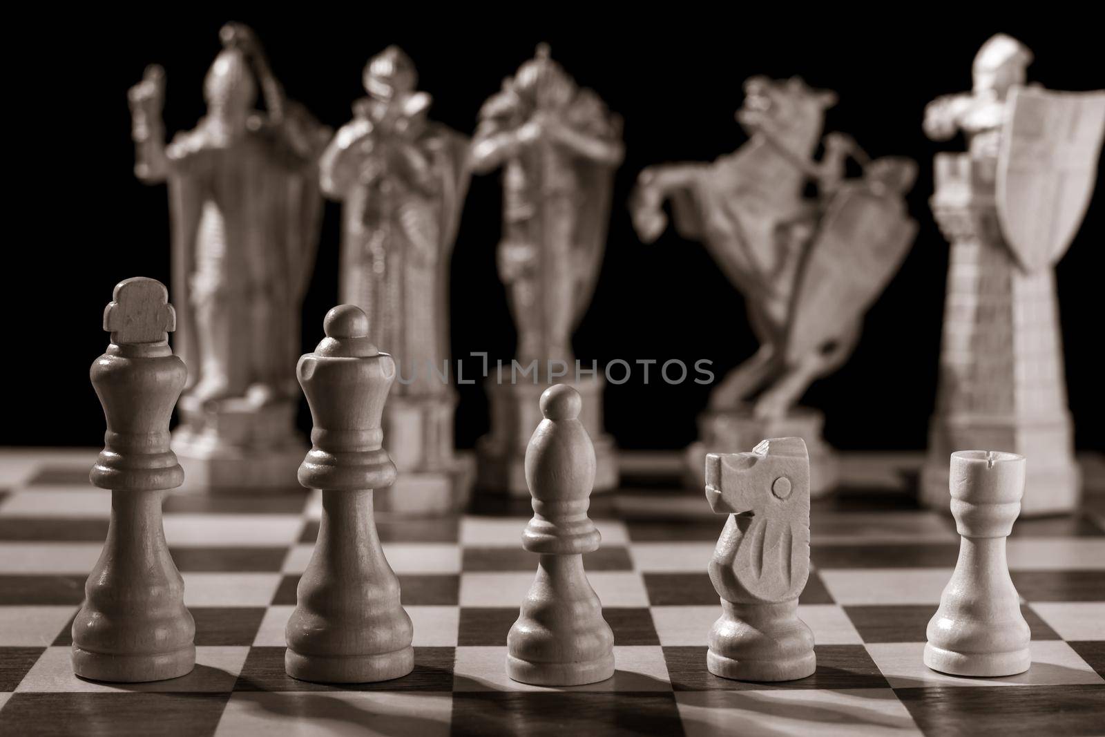 Classic white chess pieces such as king, queen, bishop, knight, rook and the same pieces in the form of medieval figures on the background. Selective focus on classic pieces