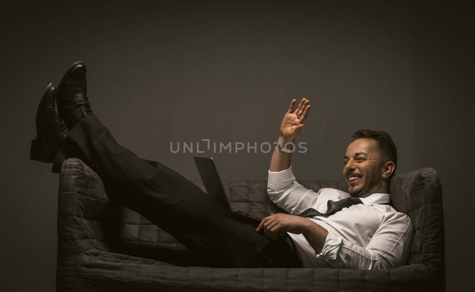 Businessman communicates using a laptop computer while lying on a sofa. Online business meeting. Work from home concept. Toned image by LipikStockMedia