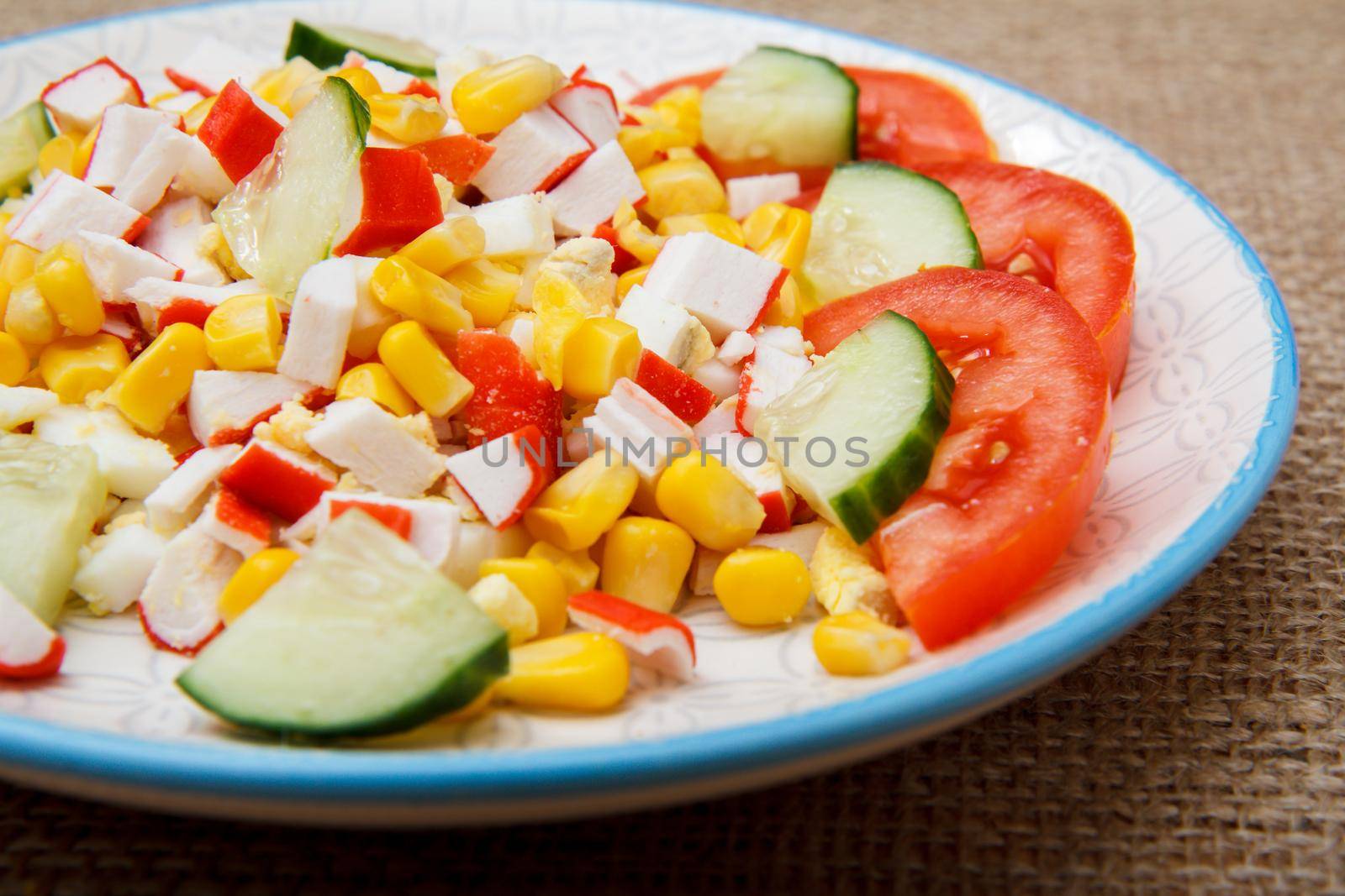 Salad with sliced crab sticks, boiled corn and fresh tomato and cucumber on plate