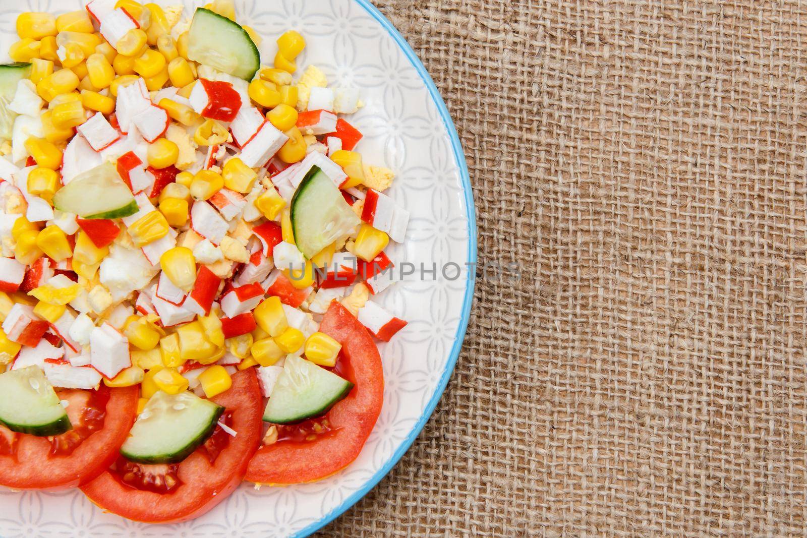 Salad with sliced crab sticks, boiled corn and fresh tomato and cucumber on plate. Top view with copy space