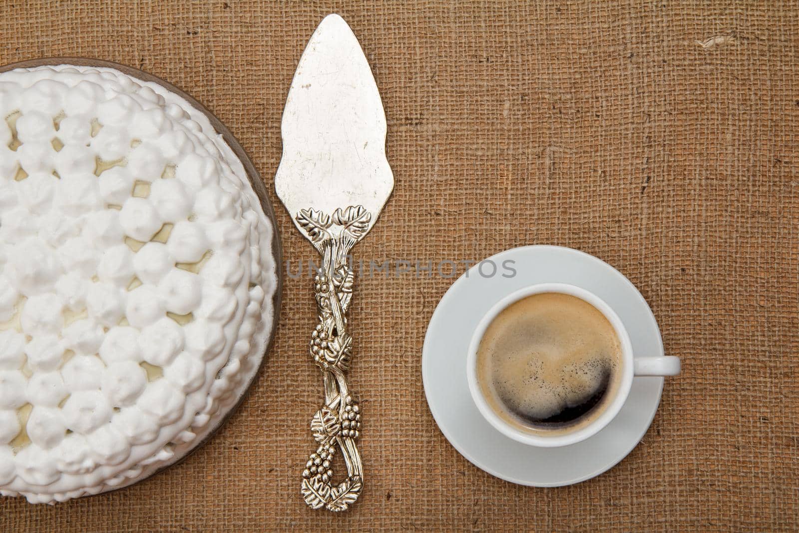 Biscuit cake decorated with whipped cream, silver cake lifter and cup of coffee on table with sackcloth. Top view