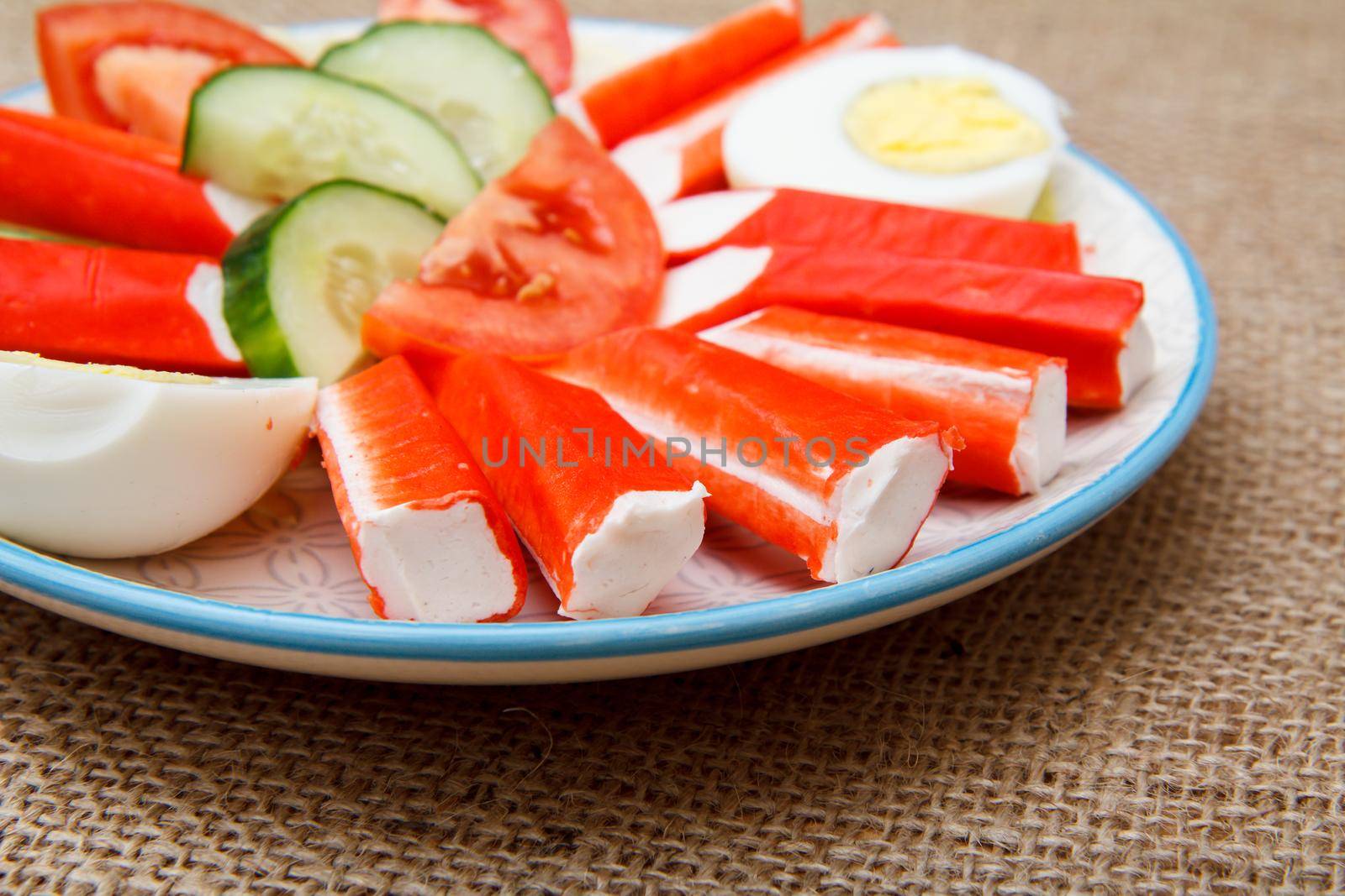Plate with crab sticks, boiled egg and freshly sliced tomato and cucumber on sackcloth