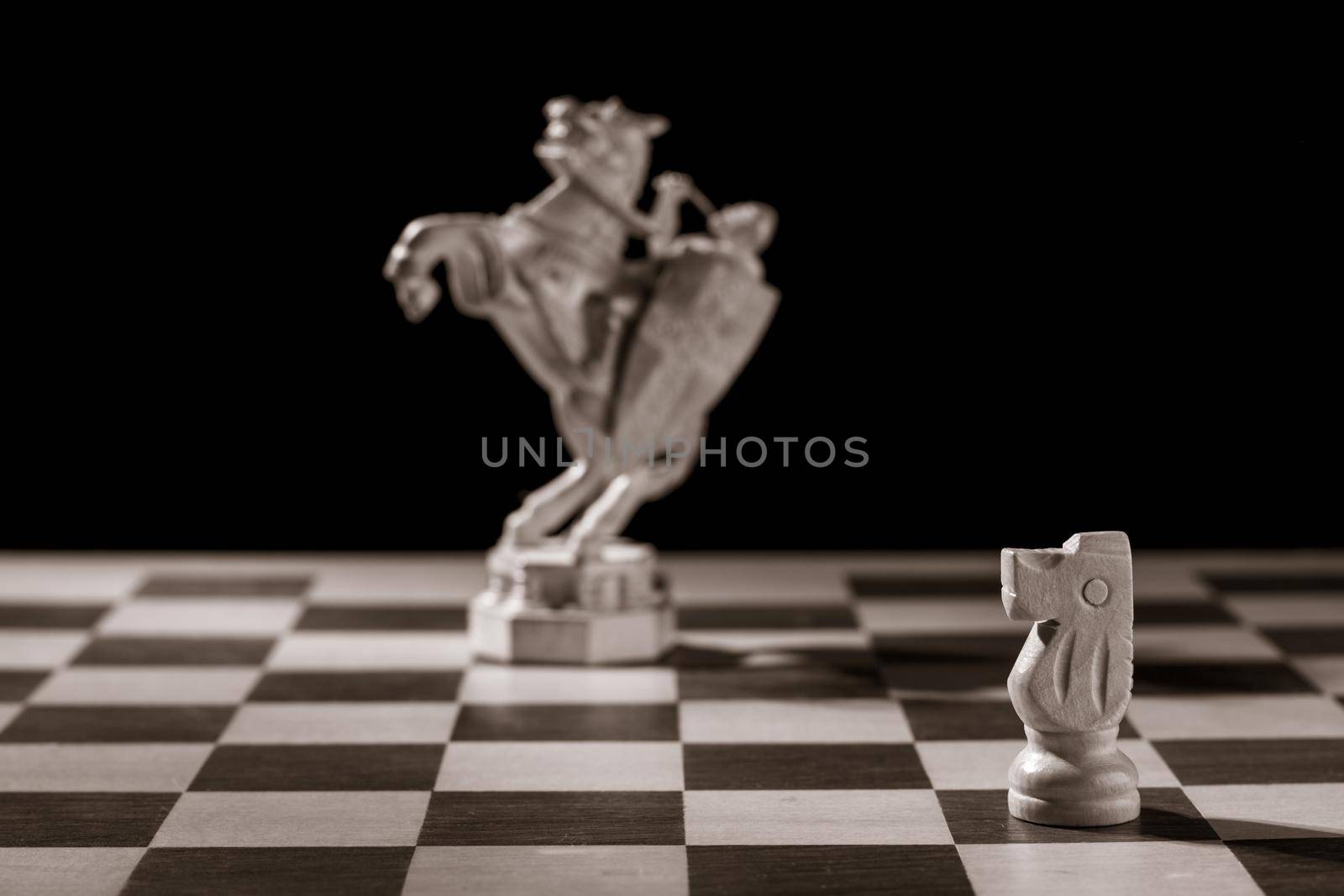 Classic white knight and the same chess piece in the form of medieval figure on the background. Selective focus on classic piece