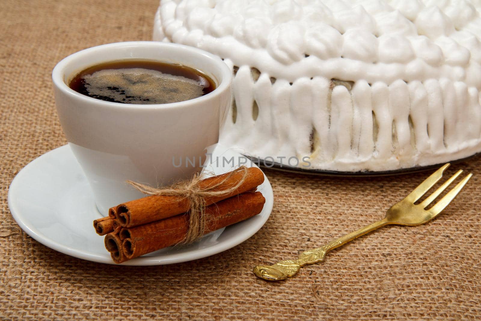 Cup of coffee, cinnamon, fork and biscuit cake decorated with whipped cream on table with sackcloth