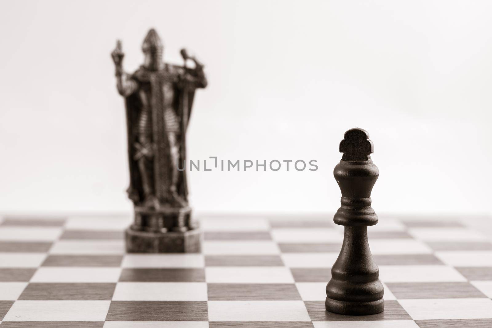 Classic black king and the same piece in the form of medieval figure on the background. Selective focus on classic piece