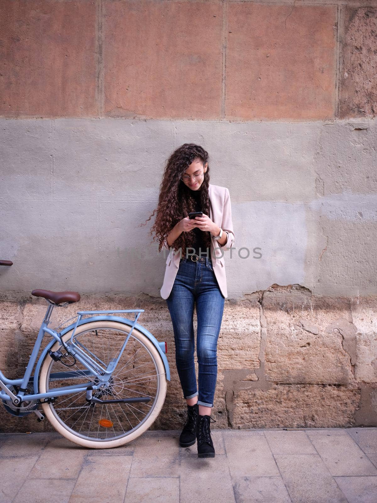 young woman looking at her mobile phone on the street next to her bike resting on her way to work. Full vertical view