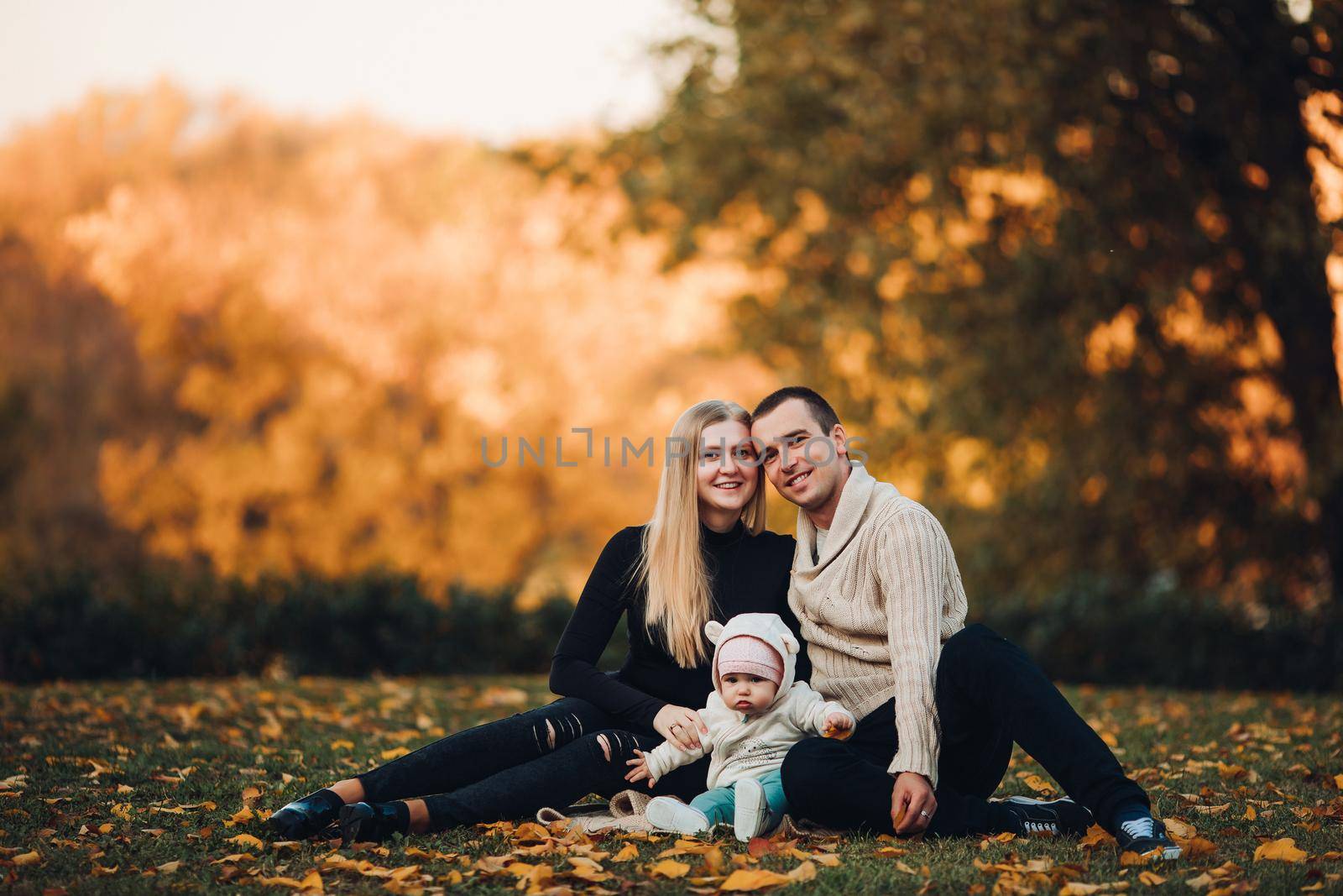 Portrait of attractive husband and blonde wife holding their surprised child. Handsome man helping pretty woman caring about little baby. Young happy family smiling at camera and standing together.