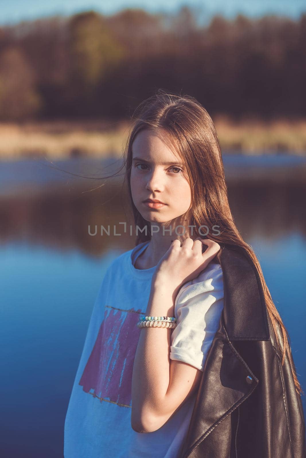 Portrait of a beautiful happy teenage girl outdoors in spring. A girl poses on lakes shore.