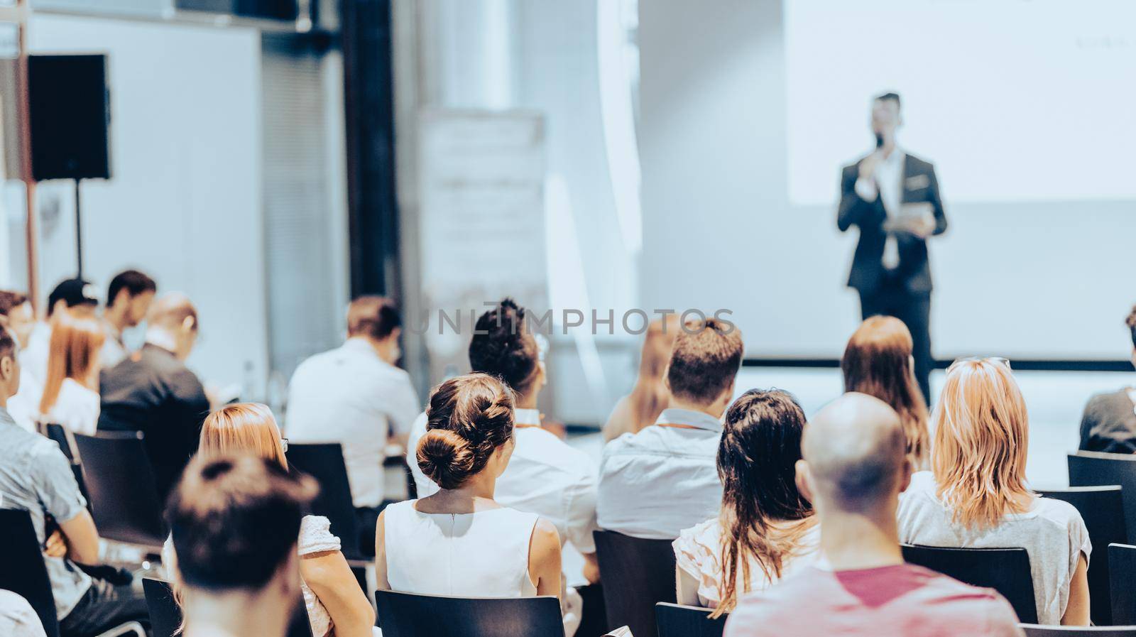 Speaker giving a talk in conference hall at business event. Rear view of unrecognizable people in audience at the conference hall. Business and entrepreneurship concept.