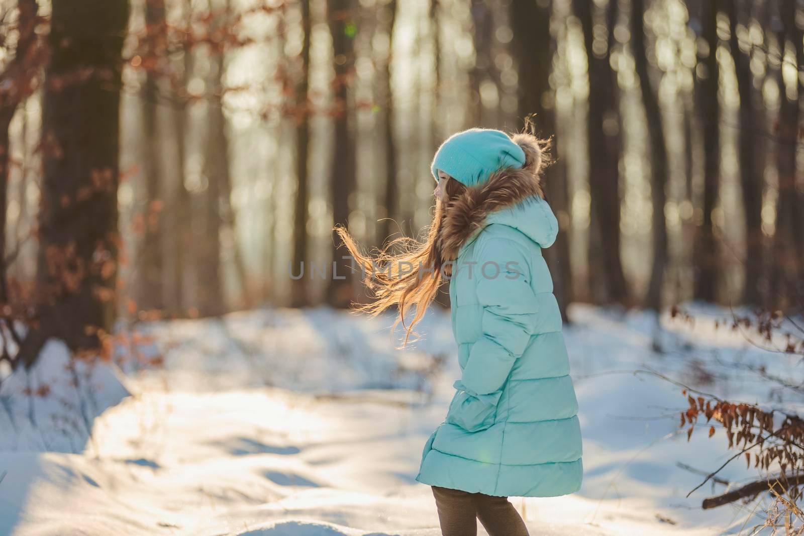 girl in a jacket and hat of turquoise color against the backdrop of a snowy forest