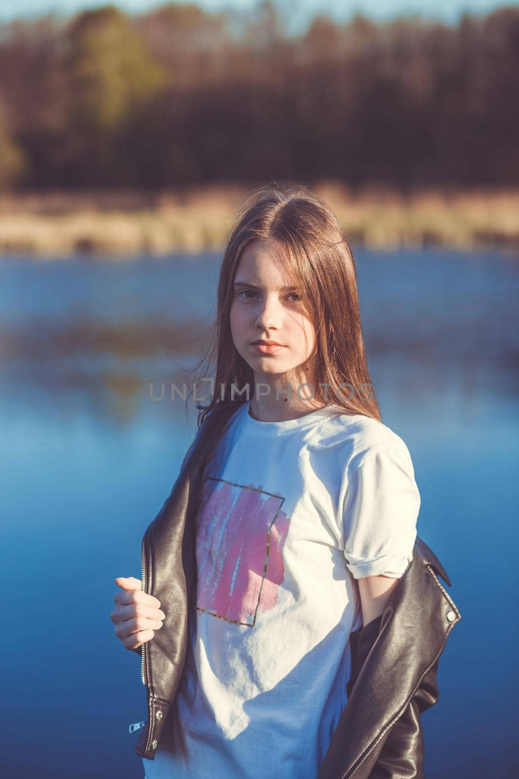 Portrait of a beautiful happy teenage girl outdoors in spring. A girl poses on lakes shore.