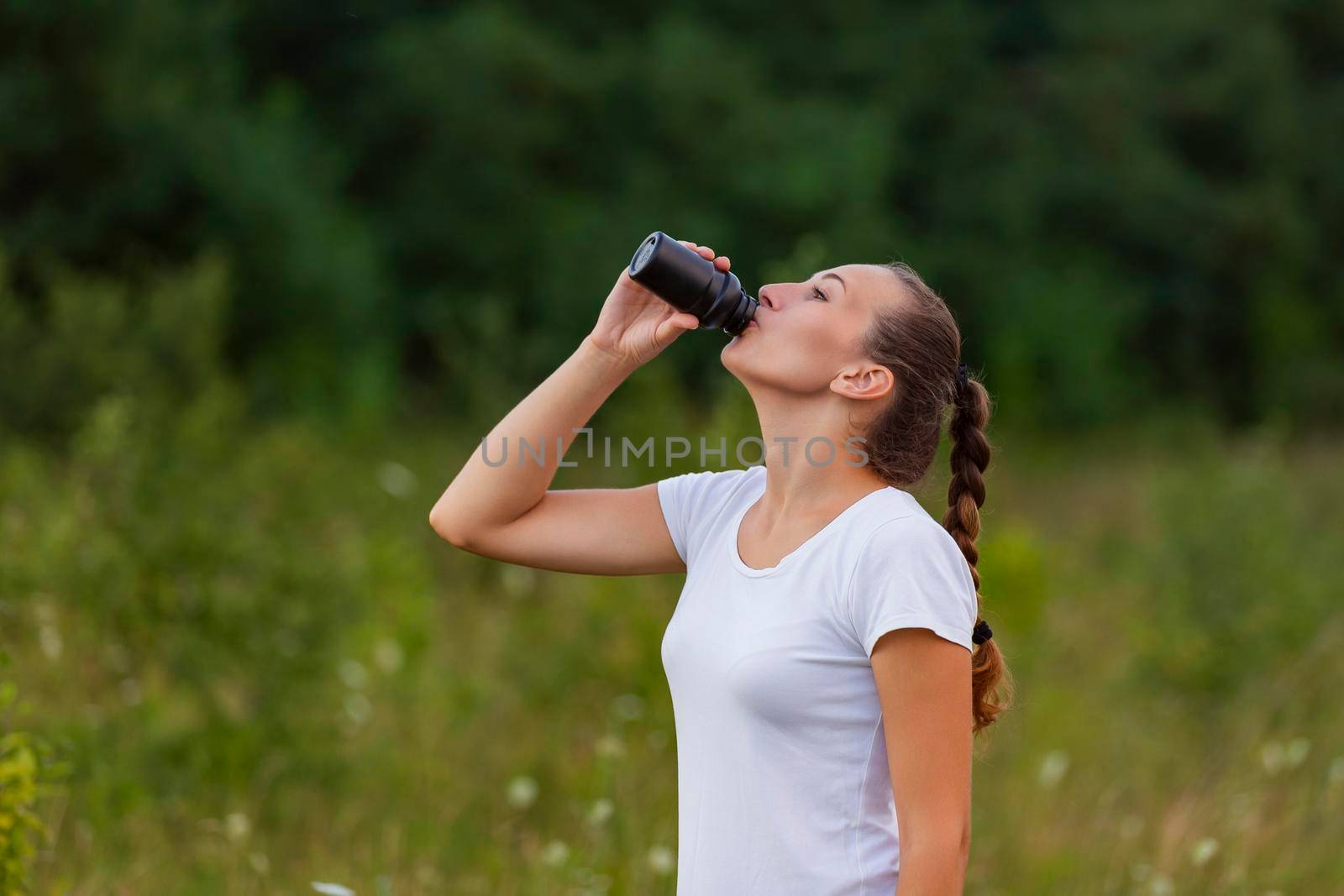 woman drinking water from a plastic bottle on the background of nature