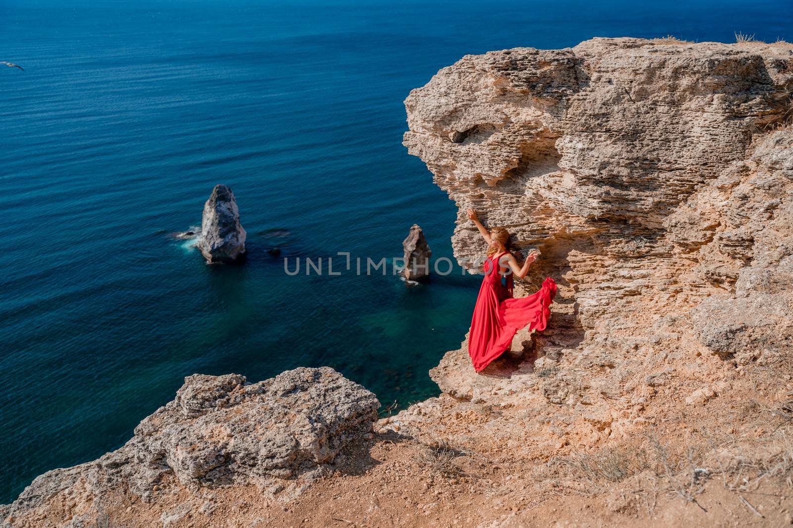 A woman in a red flying dress fluttering in the wind, against the backdrop of the sea