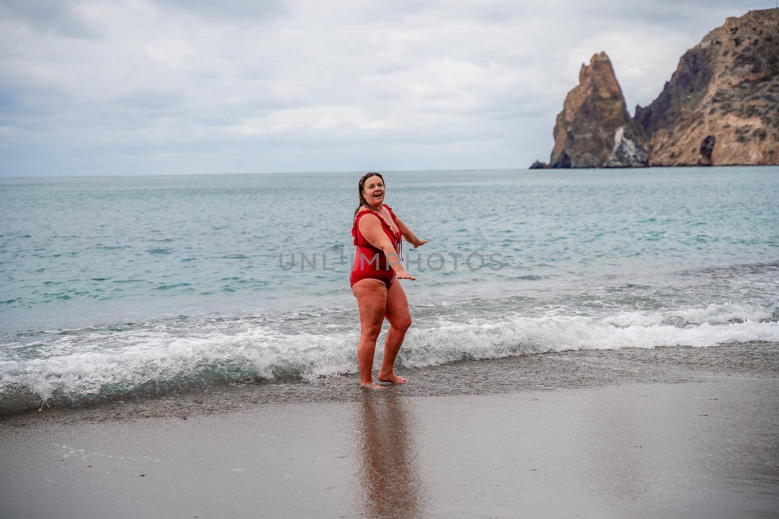 Woman in a bathing suit at the sea. A fat young woman in a red swimsuit enters the water during the surf by Matiunina