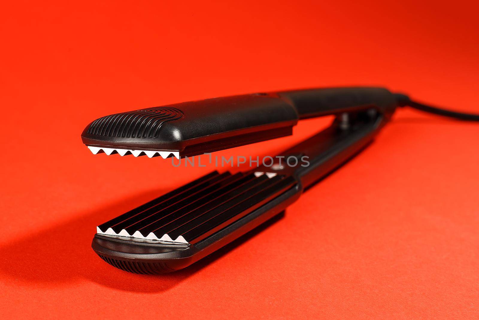 Hair corrugation iron on a red background. Barber tools, hairdressing concept