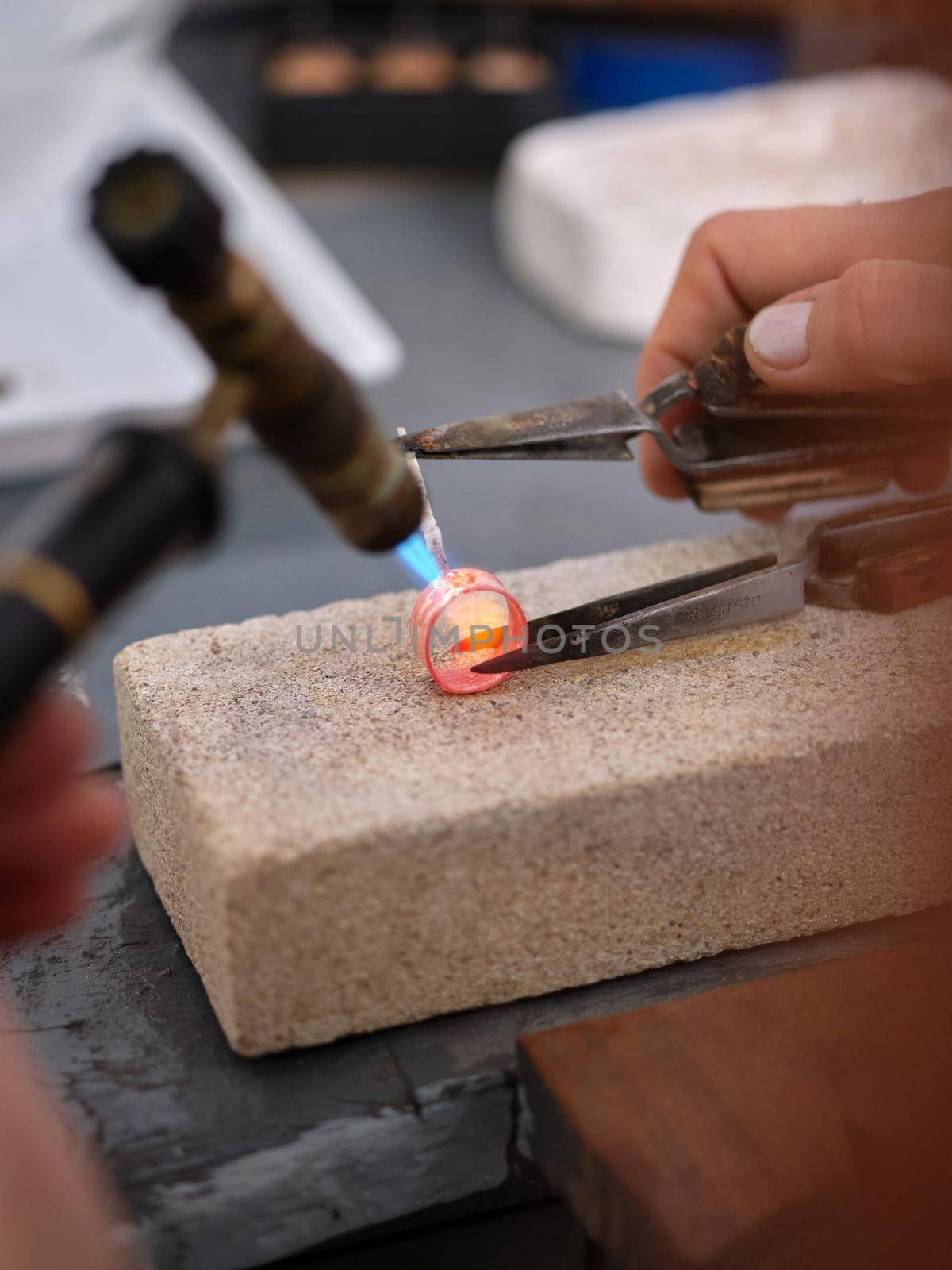 Vertical image of a woman working in her artisan jewelry workshop using a torch on a ring to perform her work on a block of stone