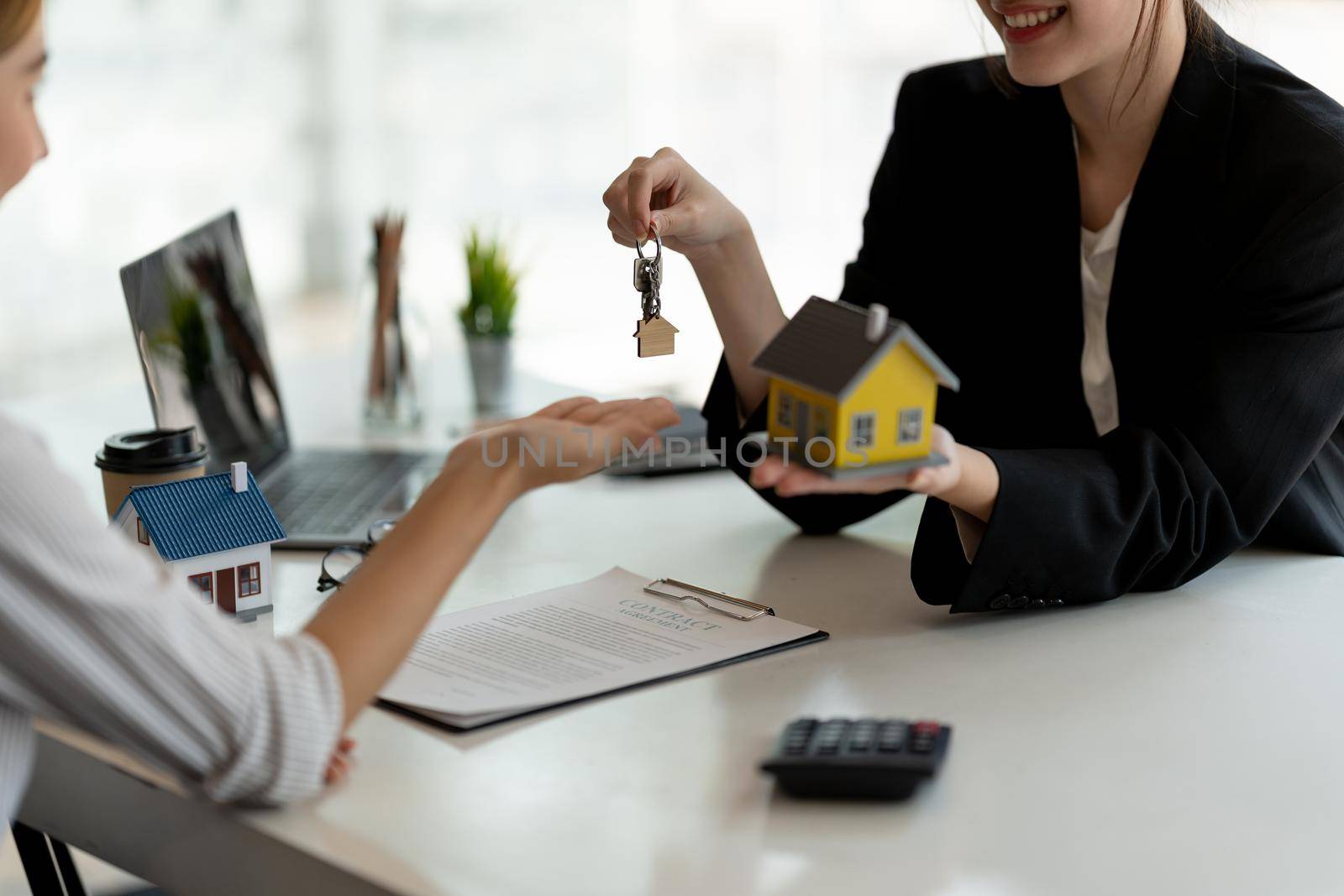 real estate agent holding house key to his client after signing contract agreement in office,concept for real estate, moving home or renting property.