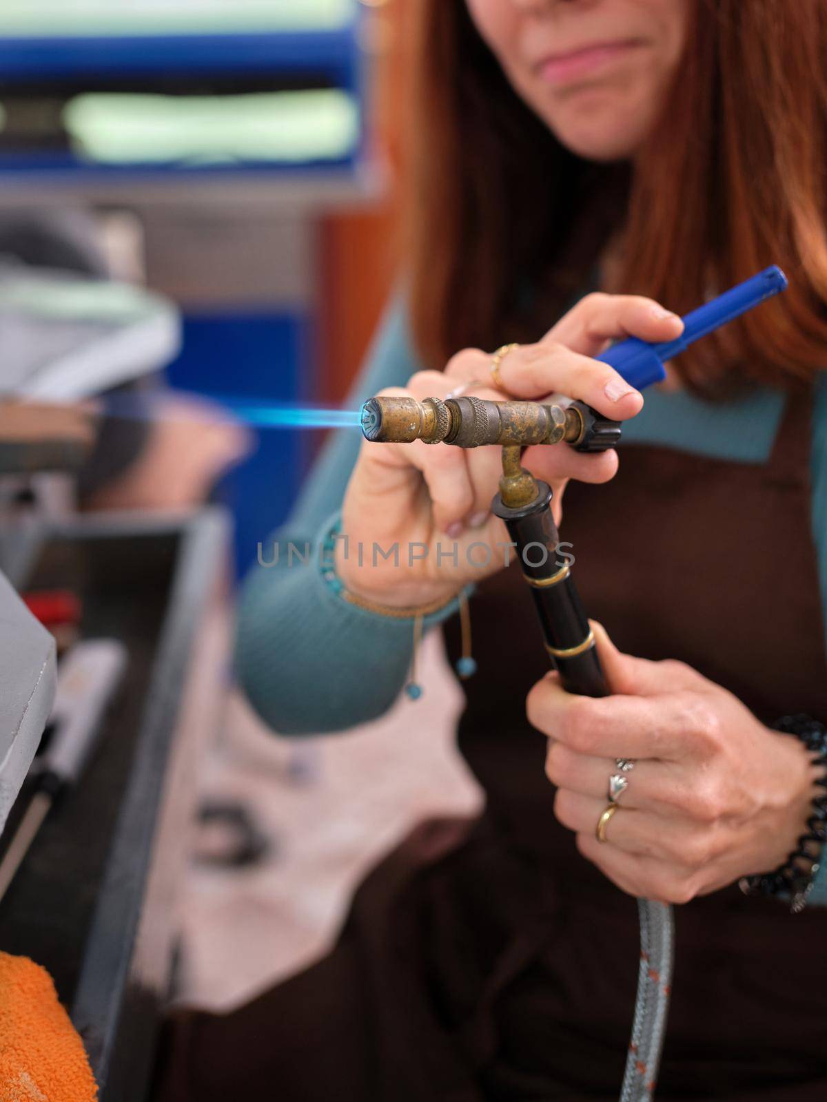 a woman working in her artisan jewelry workshop adjusting a torch to perform her work. by WesternExoticStockers