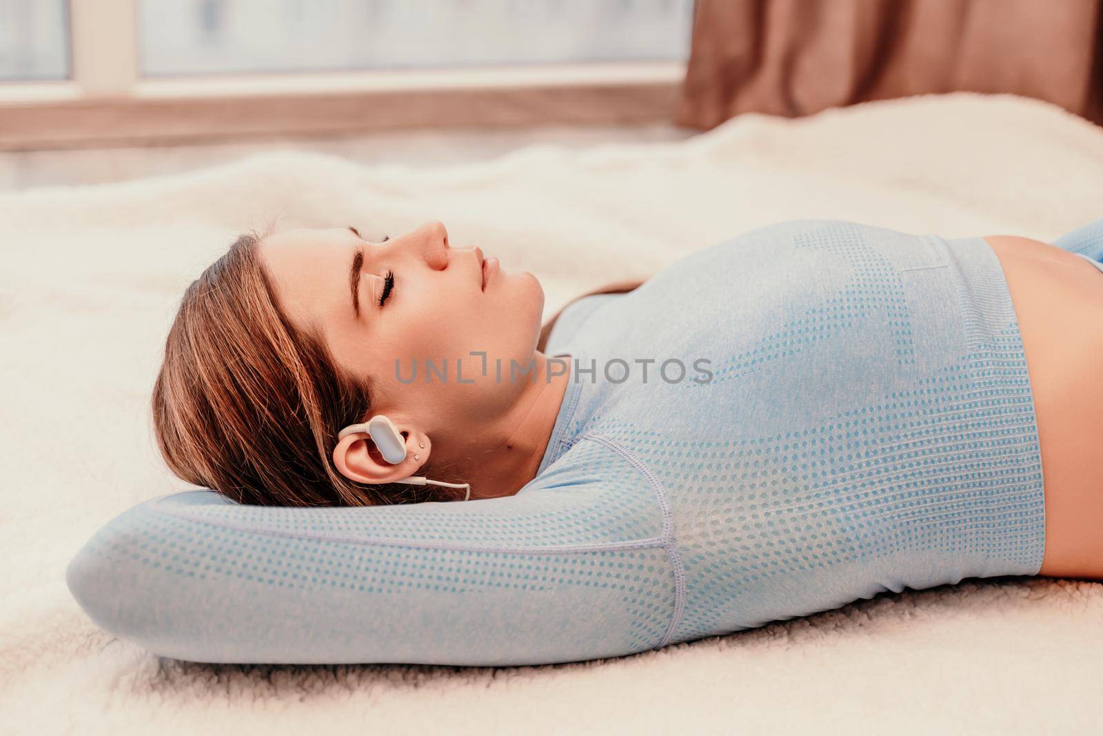 Side view portrait of relaxed woman listening to music with headphones lying on carpet at home. She is dressed in a blue tracksuit