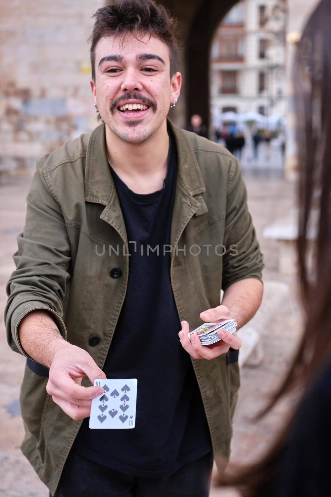 Vertical photo of a young street magician showing a card to the audience while performing a trick