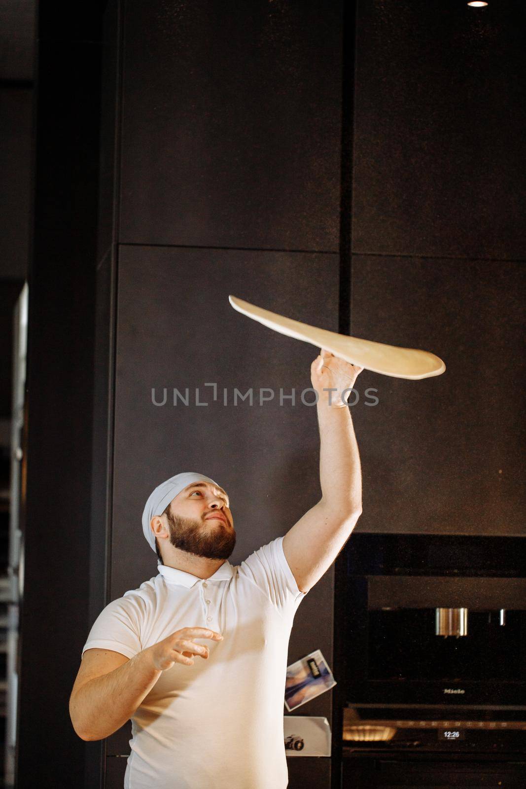 Skilled chef throwing up pizza base dough by Gravika