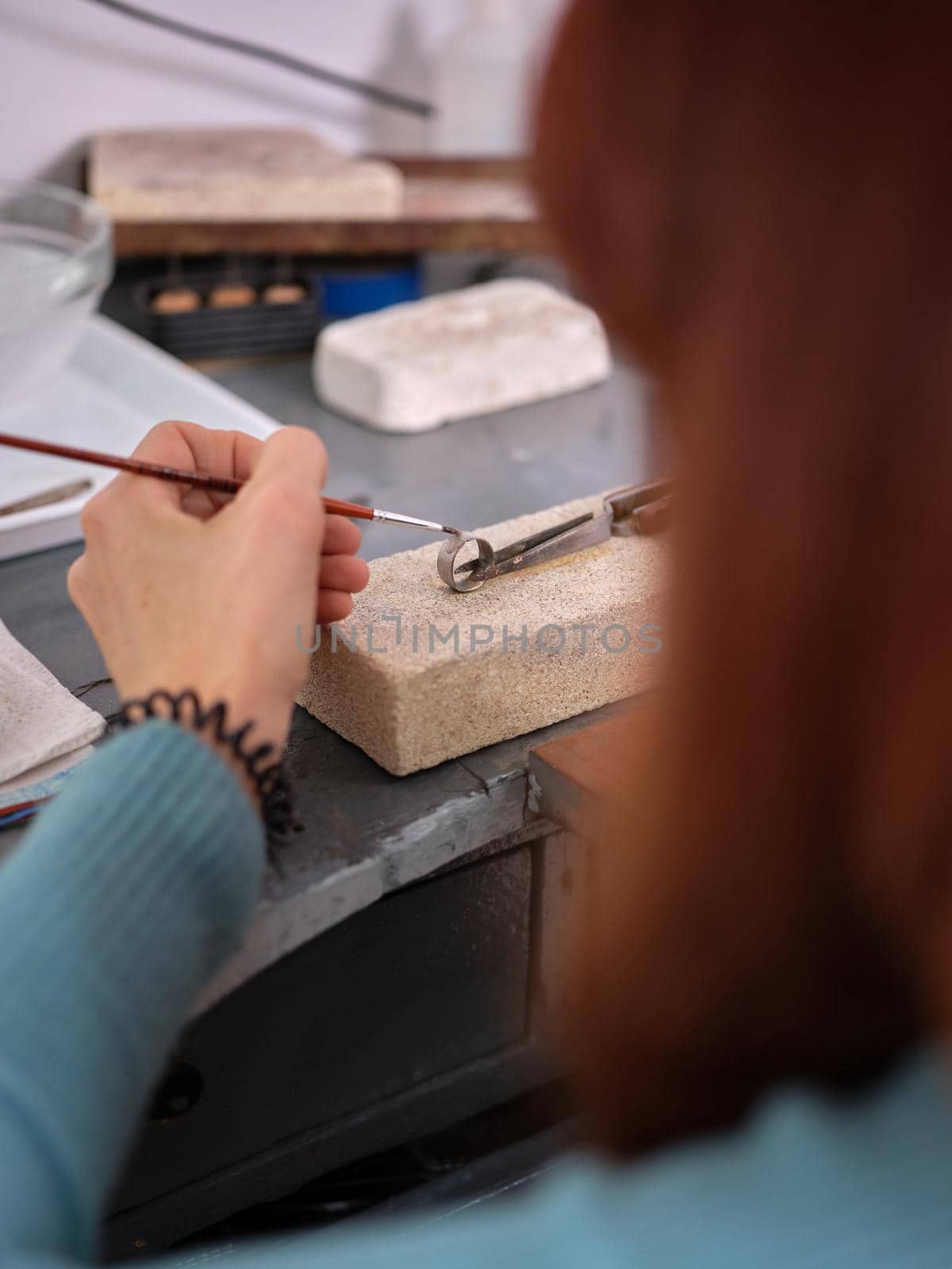 a woman working in her artisan jewelry workshop using a small brush on a ring to perform her work on a block of stone by WesternExoticStockers