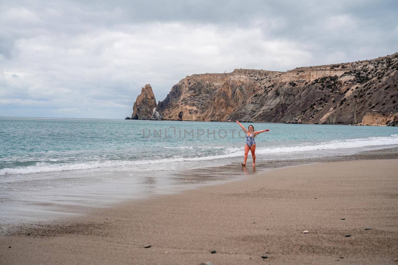 A plump woman in a bathing suit enters the water during the surf. Alone on the beach, Gray sky in the clouds, swimming in winter